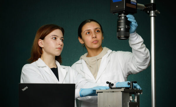 BME students Angela Mitevska (left) and Citlally Santacruz capture high-speed video of stretching a flexible bottomed 96-well plate for strain quantification in a lab.